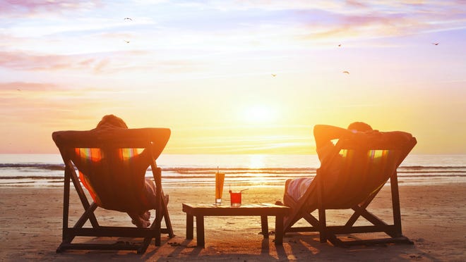 Couple relaxing in lounge chairs on a beach at sunset