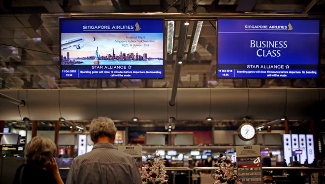 Passengers traveling on Singapore Airlines flights wait at check-in counters where advertisements for the airline's inaugural non-stop flight from Singapore to Newark is flashed on screens on Thursday, Oct. 11, 2018, in Singapore.