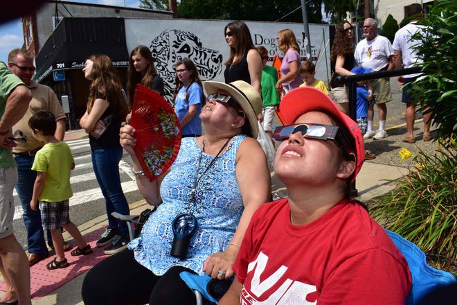 Samantha Lopez, right foreground. Saudhi Lopez, left with fan. They sit on the corner by the library with a line formed to view the eclipse through telescopes. Eclipse as viewed in front of the Boonton Library on Monday afternoon August 21, 2017.