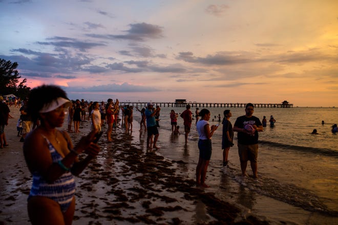 Crowds fill the beach to watch the sunset before the firework show at Naples Pier on Thursday, July 4, 2019.