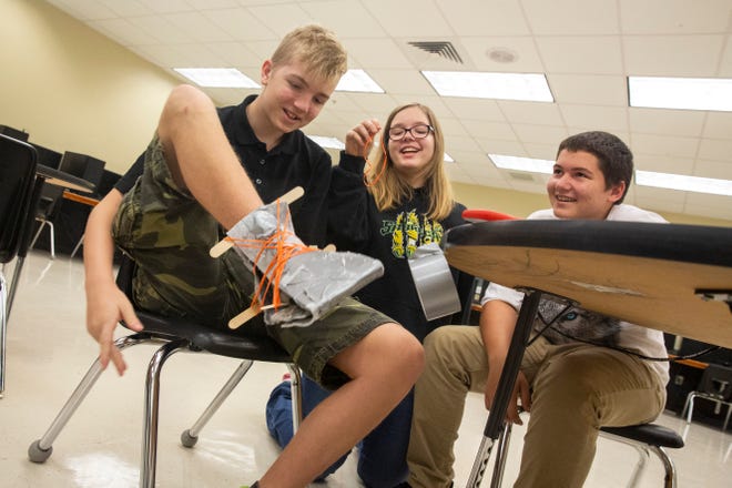 From left to right, Lucas Cristiano Hazelet, 13, Lara Rawl, 13, and Corben Freshour, 13, wrap rubber bands around a shoe they designed in a robotics class at Cypress Palm Middle School on Thursday, Aug. 29, 2019.