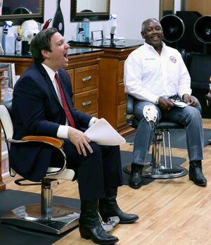 Florida Gov. Ron DeSantis, left, laughs beside Orange County Mayor Jerry Demings, right, during an appearance at the "Oh Sooo Jazzy" hair salon in Orlando, Fla., Saturday, May 2, 2020. The governor was there to discuss guidelines for reopening businesses during the coronavirus epidemic.