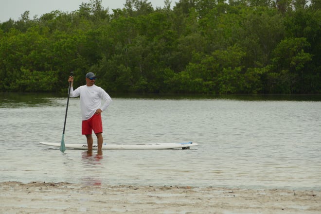A man stands next to a paddleboard at Tigertail Beach Park on July 6, 2020.
