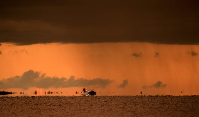 A shrimp boat heads home under a  thunderstorm and sunset over Fort Myers Beach on Tuesday, August 11, 2020.