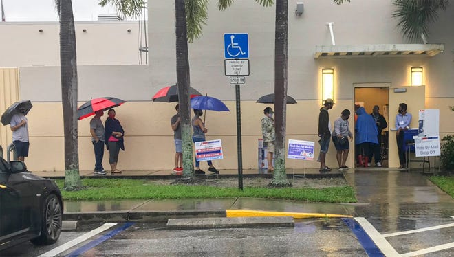 Early morning voters line up Monday under their umbrellas outside of the Wellington Library to cast their votes in the 2020 presidential election. BILL INGRAM/PALM BEACH POST