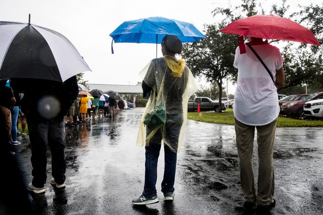 Voters including Sally Ward, center wait in a steady down pour to cast their ballot during early voting at East County Regional Library in Lehigh Acres on Monday, October 19, 2020.