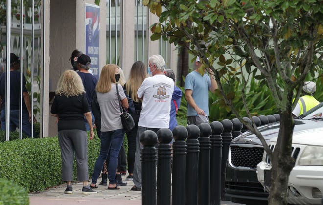 A small crowd waits outside the Martin County Supervisor of Elections office Monday, Oct. 19, 2020, as local voters head to the polls to cast their ballot on the first day of early voting in Florida. By afternoon, some of the long lines began to thin to a steady flow after rain showers passed through the county.