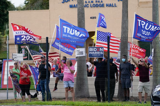 Supporters of President Donald Trump wave flags and shout outside a campaign rally as one man holds a Biden Harris sign where former President Barack Obama spoke to a crowd that supported Democratic presidential candidate former Vice President Joe Biden Tuesday, Oct. 27, 2020, in Orlando, Fla.