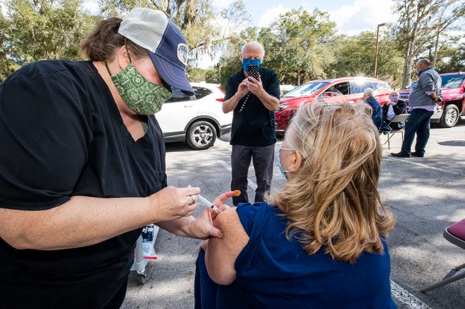 Kelly Conklin, left, an RN and epidemiology and immunization supervisor for the Marion County Health Dept., gives Sandi Johnson, right, her COVID-19 Moderna vaccine Tuesday afternoon, January 5, 2021 at the Marion County Health DepartmentÕs parking lot in Ocala, FL. as her husband Ron Johnson takes her picture. The shots were for people who are 65 and over who had an appointment. The health department had scheduled 60 people an hour and hoped to vaccinate about 200 people on Tuesday. The patients will return to the Paddock Mall on February 2nd for their second and final shot. The Marion County Health Department already has about 50,000 people registered for the vaccine. [Doug Engle/Ocala Star Banner]2021