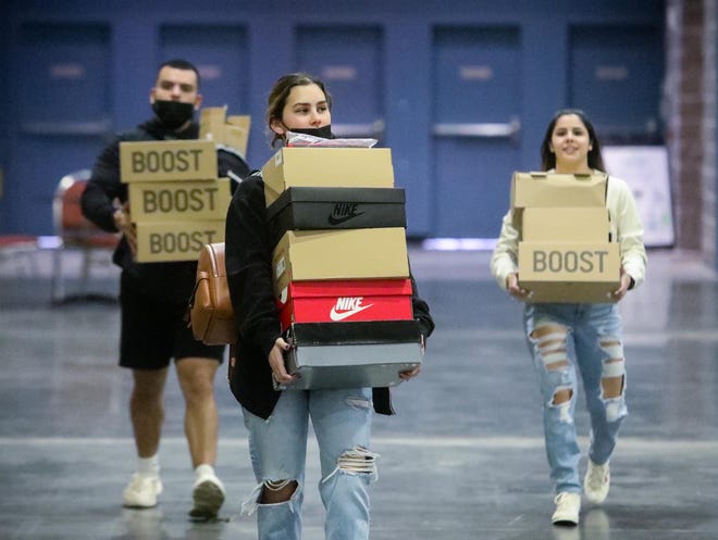 (from left) Lazaro Aguiar, Helen Yanes, an Anelys Rodriguez of the Hypehia shoe company carry boxes of shoes at the start of the Sneaker Exit trade show at the Palm Beach Convention Center Sunday, January 16, 2022.